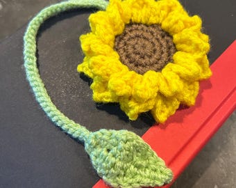 May include: A crocheted sunflower bookmark with a green stem and leaf. The sunflower is yellow with a brown center.