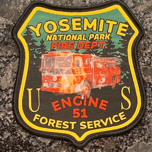 Puede incluir: Un parche bordado negro y amarillo con el texto "Yosemite National Park Fire Dept. U.S. Engine 51 Forest Service". El parche presenta un camión de bomberos rojo con llamas.