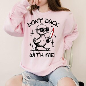 Pode incluir: Uma camisa de moletom rosa com o texto "Don't Duck With Me!" e um pato de desenho animado usando &oacute;culos de sol e segurando uma faca ensanguentada.