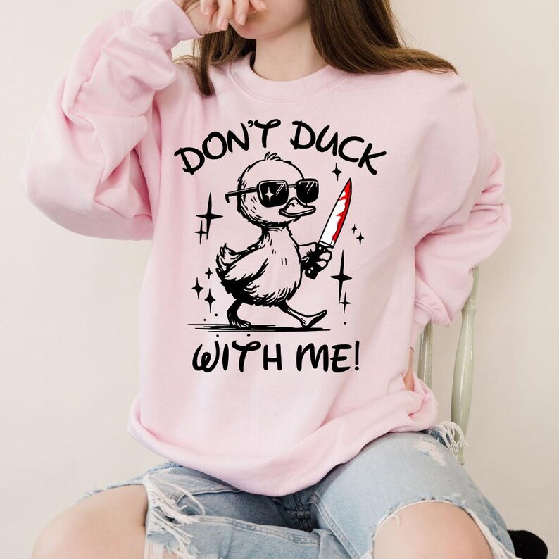 Pode incluir: Uma camisa de moletom rosa com o texto "Don't Duck With Me!" e um pato de desenho animado usando &oacute;culos de sol e segurando uma faca ensanguentada.