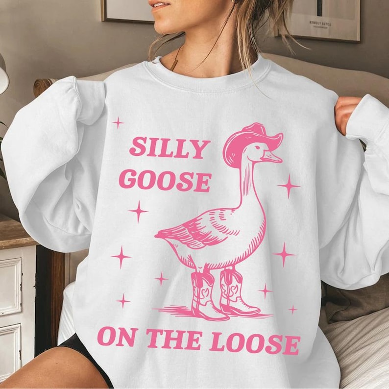 May include: White sweatshirt with a pink graphic of a goose wearing a cowboy hat and boots. The text "Silly Goose on the Loose" is printed below the goose.