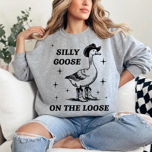 May include: A gray sweatshirt with the text "Silly Goose on the Loose" and a cartoon goose wearing a cowboy hat and boots.