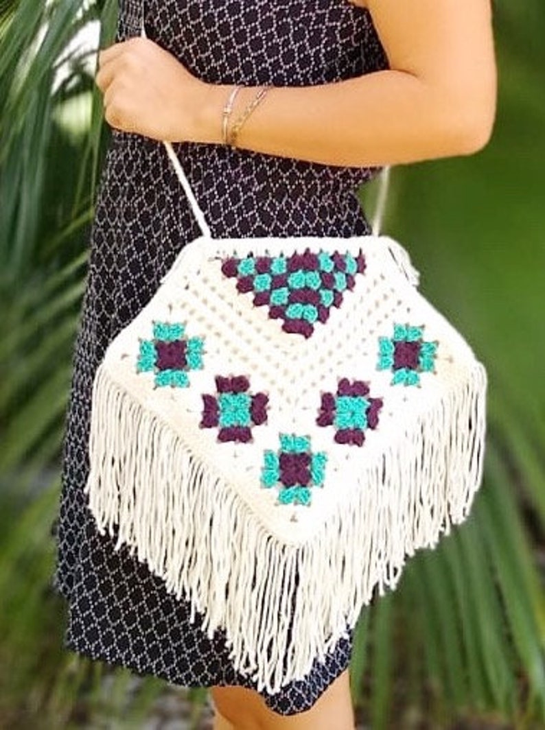 May include: White crocheted shoulder bag with a geometric pattern in teal and purple. The bag has a long fringe around the bottom.