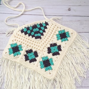 May include: A white crochet top with a geometric pattern in teal and brown. The top has a fringe trim.