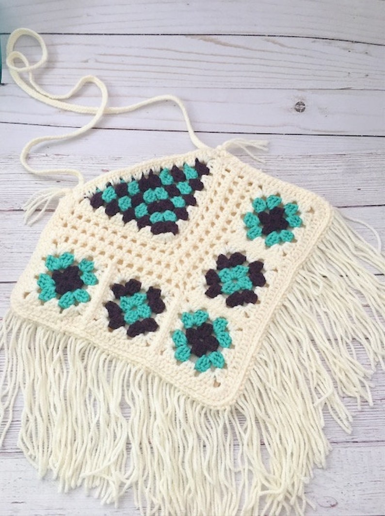 May include: A white crochet top with a geometric pattern in teal and brown. The top has a fringe trim.