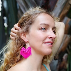 May include: A pair of pink tassel earrings with a geometric design. The earrings are made of a thin, silver wire and have a fringe of pink tassels.