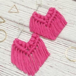 Może przedstawiać: Para r&oacute;żowych kolczyk&oacute;w z frędzlami z srebrnymi k&oacute;łkami. Kolczyki są wykonane z makramu i mają frędzlowany wz&oacute;r.