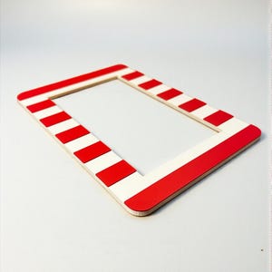 May include: A rectangular picture frame with a red and white striped pattern. The frame is made of wood and has a clean, modern design. The red stripes alternate with white stripes around the frame.
