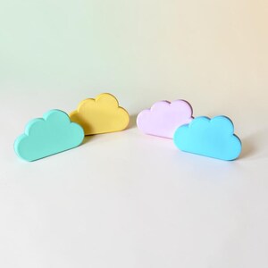 May include: Four cloud-shaped objects in pastel colors. The set includes one mint green, one yellow, one light purple, and one bright blue cloud. Each piece has a smooth, matte finish and a rounded, puffy silhouette with a flat base for standing.