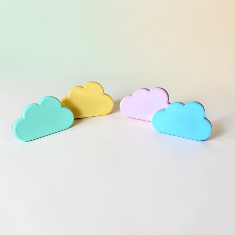 May include: Four cloud-shaped objects in pastel colors. The set includes one mint green, one yellow, one light purple, and one bright blue cloud. Each piece has a smooth, matte finish and a rounded, puffy silhouette with a flat base for standing.