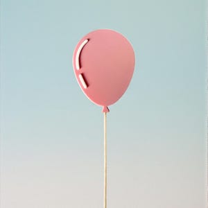 May include: A pink balloon-shaped decoration with white accents and a string. The balloon is set against a gradient blue background. The balloon's design includes a curved line and a straight line.