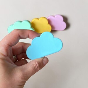 May include: A set of four cloud-shaped objects in pastel colors including light blue, mint green, yellow, and pink. Each cloud has a smooth, matte finish and a rounded, scalloped edge design. The objects are arranged in a small cluster.