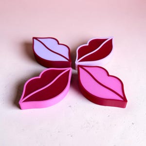 May include: Four lip-shaped objects arranged in a cluster. Each piece features a distinct color combination: light purple with dark red, dark red with light purple, dark red with bright pink, and bright pink with dark red.