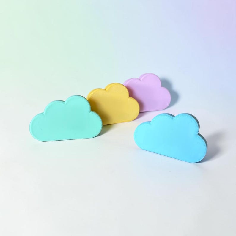 May include: Four cloud-shaped objects in pastel colors. One is mint green, one is yellow, one is light purple, and one is sky blue. Each object has a smooth, rounded surface and a flat base, arranged in a staggered formation on a white surface.