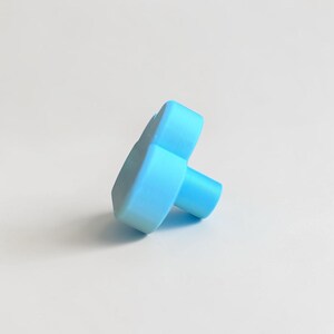 May include: A light blue cabinet knob shaped like a cloud. The knob features a smooth, matte finish with a rounded, puffy silhouette and a cylindrical base extending from the back, designed for attachment to furniture or cabinetry doors.