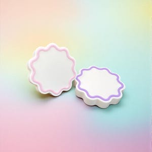 Pode incluir: Duas bases brancas com bordas onduladas e acabamentos em rosa pastel e roxo. As bases estão em um fundo gradiente de rosa, amarelo e azul. As bases têm um design simples e limpo.