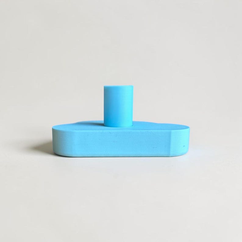 May include: A bright light blue candle holder featuring a smooth, matte finish. The object consists of a flat, cloud-shaped base with a single, centered cylindrical pillar extending upward, designed to securely hold a standard taper candle.