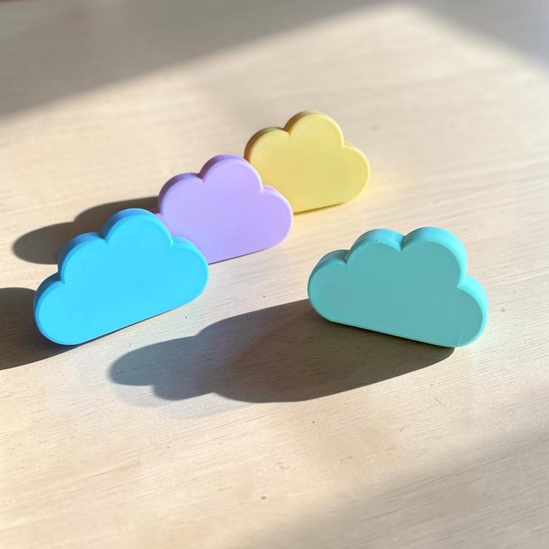 May include: Four cloud-shaped objects in pastel colors, including light blue, lavender, pale yellow, and mint green. Each piece has a smooth, solid finish and a rounded, multi-lobed top edge, arranged in a staggered formation on a flat surface.