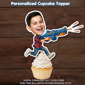 May include: A personalized cupcake topper featuring a cartoon-style illustration of a person with a large head, wearing a red and blue plaid shirt and blue jeans, holding a blue toy blaster that shoots orange darts, positioned atop a frosted cupcake.