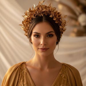 May include: A woman wearing a gold-colored leaf crown and a matching gold dress with embroidered floral details. The crown is made of multiple gold leaves. The dress has a V-neck and flowing sleeves.