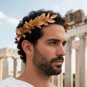 May include: A gold-colored laurel wreath made of leaves, worn on dark curly hair. The person is wearing a white toga. The background features ancient Roman columns and a blue sky.