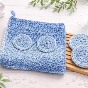 May include: A blue and white ombre crochet washcloth with two matching round crochet pads attached. Three additional crochet pads sit on a wooden holder. The items are part of a spa or bath set.