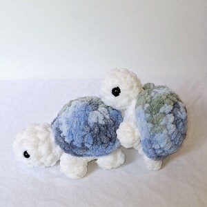 May include: Two crocheted plush turtle toys. One turtle is white with a blue and green shell. The other turtle is white with a blue shell.