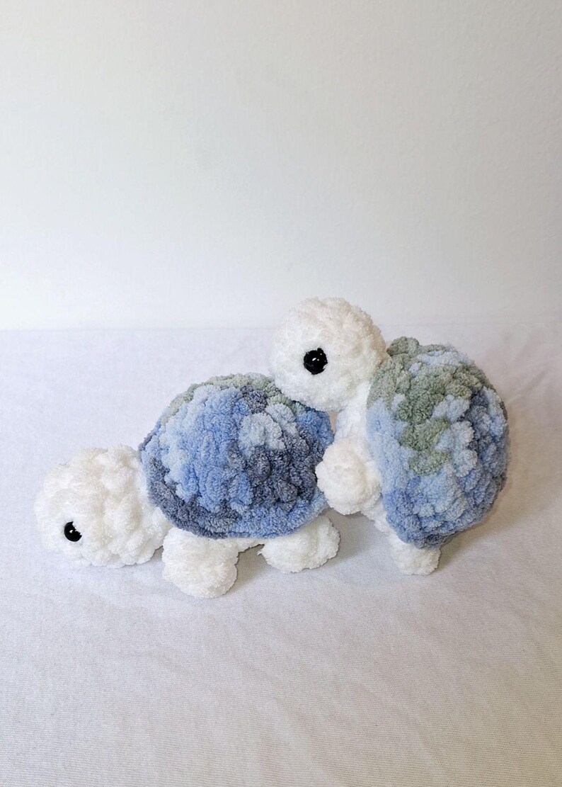 May include: Two crocheted plush turtle toys. One turtle is white with a blue and green shell. The other turtle is white with a blue shell.