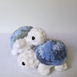May include: Two crocheted stuffed turtle toys. One is white with blue and gray shell, the other is white with green and gray shell.