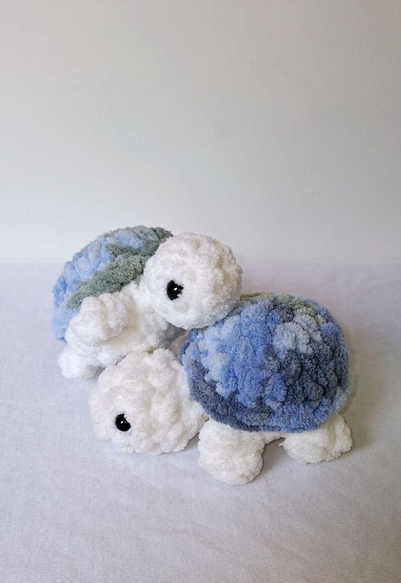 May include: Two crocheted stuffed turtle toys. One is white with blue and gray shell, the other is white with green and gray shell.