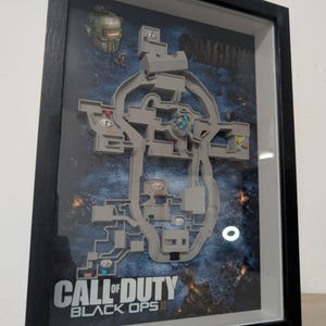 Könnte beinhalten: Gerahmtes Kunstwerk mit einer detaillierten Karte aus dem Videospiel "Call of Duty: Black Ops II - Origins". Die Karte ist grau und vor einem dunkelblauen und schwarzen Hintergrund platziert. Das Kunstwerk ist in einem schwarzen Rahmen eingefasst.