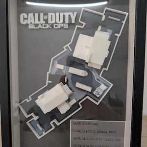 Puede incluir: Obra de arte enmarcada con el mapa Nuketown de Call of Duty: Black Ops. El mapa es un modelo 3D en blanco, sobre un fondo gris. El marco incluye el título del juego y la información de lanzamiento. La obra está encerrada en un marco negro.