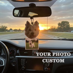 Puede incluir: Ambientador de coche personalizado con la cara de un perro y una foto de un perro en una peque&ntilde;a tarjeta cuadrada. El texto "YOUR PHOTO CUSTOM" es visible en el salpicadero. El fondo muestra una puesta de sol sobre una carretera.