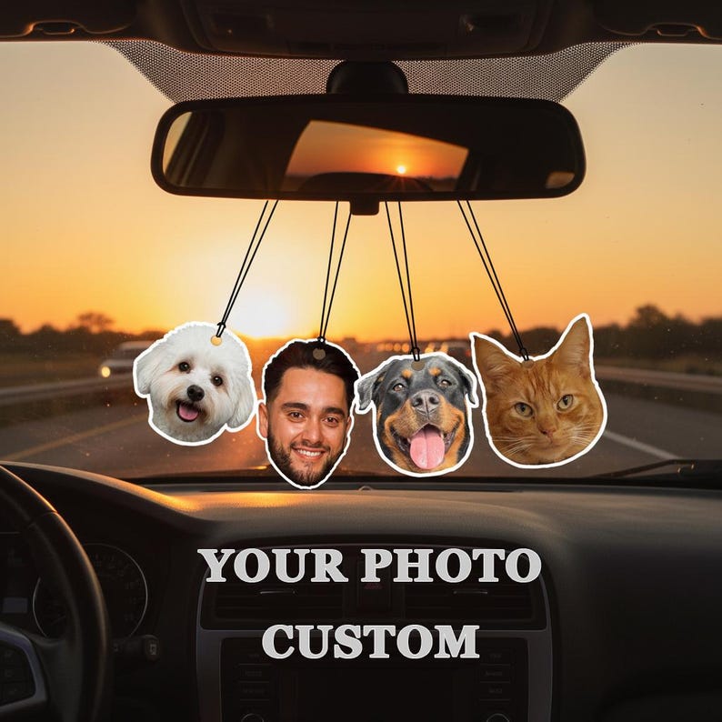 Puede incluir: Ambientadores de coche personalizados con un perro blanco, un hombre, un Rottweiler y un gato naranja, colgados del espejo retrovisor. El salpicadero muestra el texto "YOUR PHOTO CUSTOM". El fondo muestra una puesta de sol.