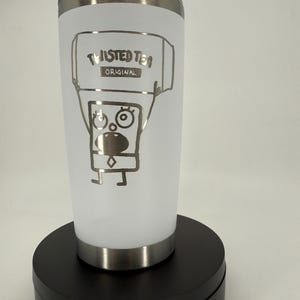 May include: White insulated tumbler with a silver rim and lid. The tumbler features a silver graphic of a cartoon character holding a sign that reads "Twisted Tea Original."