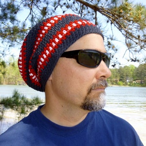 May include: A gray, red, and white crocheted beanie with a slouchy fit. The beanie is worn by a person with a beard and sunglasses.