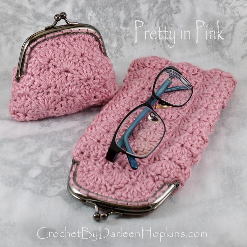 K&ouml;nnte beinhalten: Eine rosa geh&auml;kelte Geldb&ouml;rse mit einem Metallverschluss und ein passendes rosa geh&auml;keltes Brillenetui. Der Text "Pretty in Pink" steht &uuml;ber den Geldb&ouml;rsen.