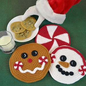 Puede incluir: Cuatro posavasos de crochet con temática navideña: un hombre de jengibre, un muñeco de nieve, un bastón de caramelo y un plato de galletas. Los posavasos son blancos, marrones, rojos y verdes.