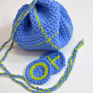Puede incluir: Una bolsa de cord&oacute;n de crochet azul con ribete verde y dos c&iacute;rculos de crochet a juego. La bolsa tiene un cord&oacute;n largo que tambi&eacute;n est&aacute; tejido en crochet azul y verde.
