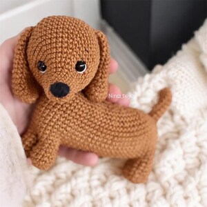 Puede incluir: Un juguete de cachorro de dachshund de crochet marrón con ojos negros y nariz negra.