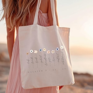 May include: Cream-colored tote bag with a floral design and German text. The bag features a row of colorful flowers and the words "Liebe, Freude, Friede, Geduld, Freundlichkeit, G&uuml;te, Treue, Sanftmut, Selbstbeherrschung" and "Galater 5: 22-23".