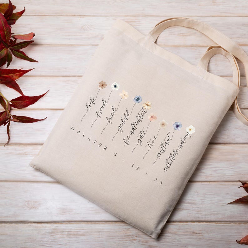 May include: Beige canvas tote bag with a floral design and German text. The bag features a series of watercolor flowers and the words "Liebe, Freude, Friede, Geduld, Freundlichkeit, G&uuml;te, Treue, Sanftmut, Selbstbeherrschung" and "Galater 5:22-23".