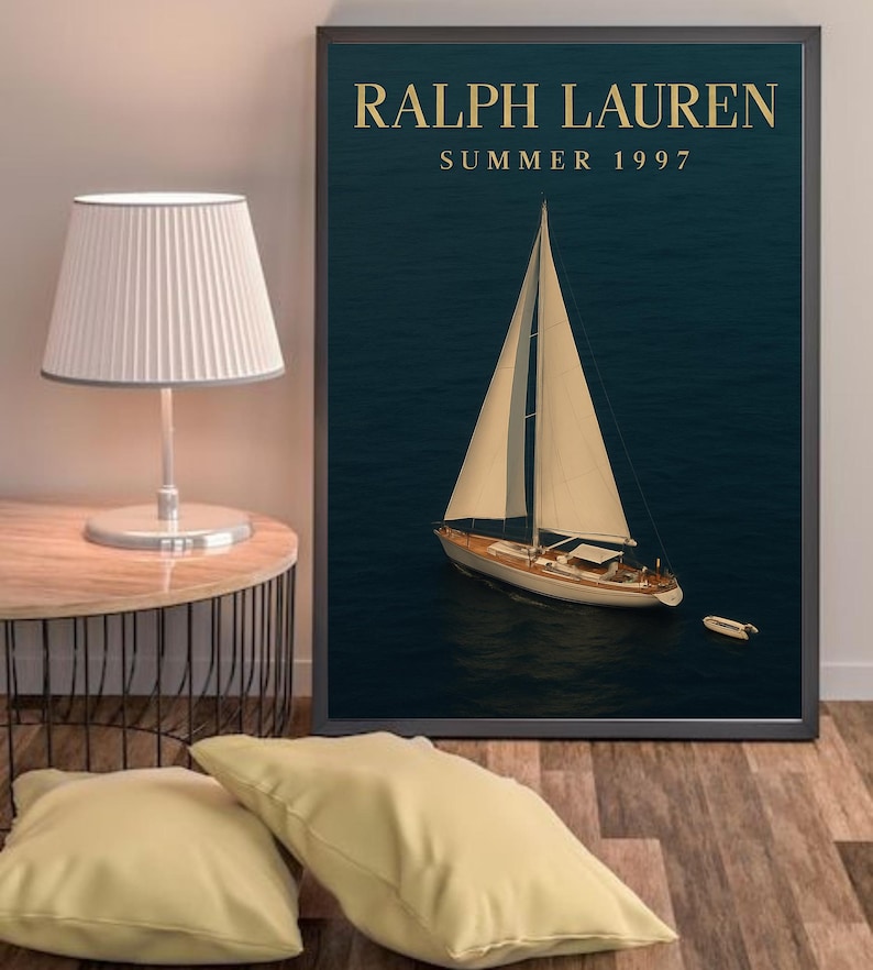 Op de afbeelding: Een ingelijste print met een zeilboot op een donkerblauwe zee. De tekst "RALPH LAUREN SUMMER 1997" staat in gouden letters. De zeilboot heeft witte zeilen en een houten romp. Een kleine boot is in de buurt zichtbaar.
