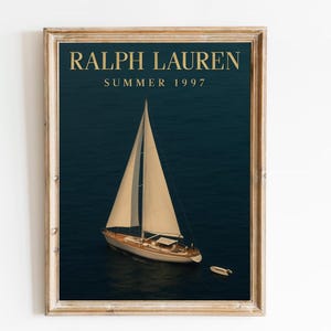 Op de afbeelding: Ingelijste print met een zeilboot op een donkerblauwe zee. De print heeft de tekst "RALPH LAUREN SUMMER 1997" in gouden letters. De lijst is lichtbruin.