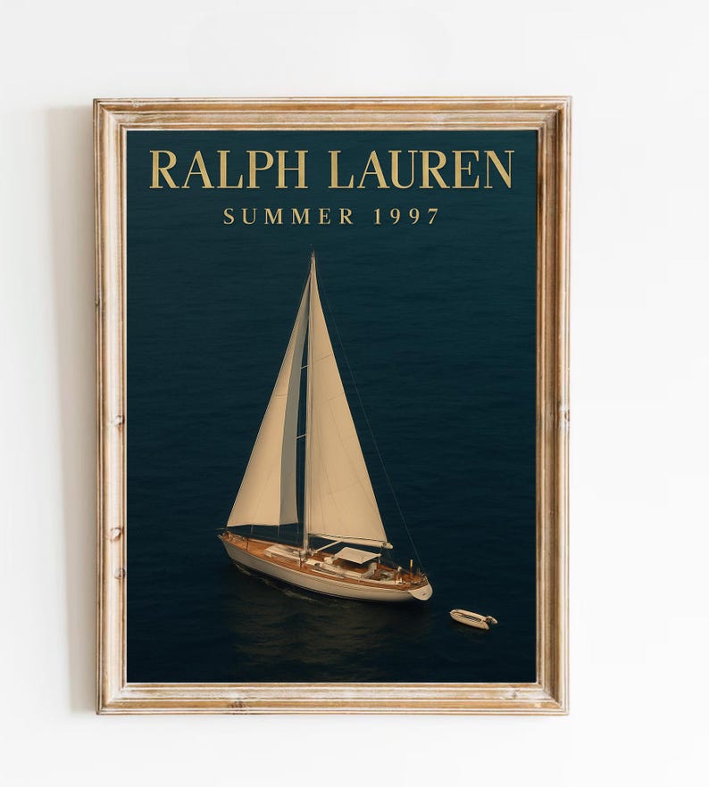 Op de afbeelding: Ingelijste print met een zeilboot op een donkerblauwe zee. De print heeft de tekst "RALPH LAUREN SUMMER 1997" in gouden letters. De lijst is lichtbruin.