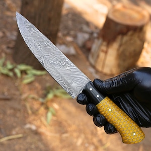Peut inclure: Un couteau de chef en acier Damas avec un manche en nid d'abeille jaune. Le couteau a un manche noir avec des points blancs.