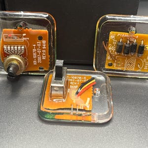 May include: Three clear, square electronic components with orange circuit boards are displayed. Each component has different electronic parts, including a potentiometer, a switch, and diodes. The components have text that reads "KR-1087B-4", "2007-07-03", and "REV:0 94HB".