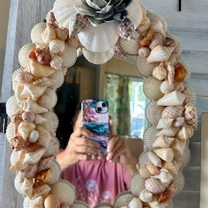 Coastal oval wall mirror, handmade with multiple seashells and a floral seashell accent great for beach house wall art or entry way.