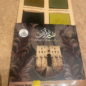 May include: A set of three Aleppo soap bars in a box. The soap bars are green and brown and have a tree design on them. The box is brown and has the words "Sham Shareef" and "Aleppo Soap" on it.