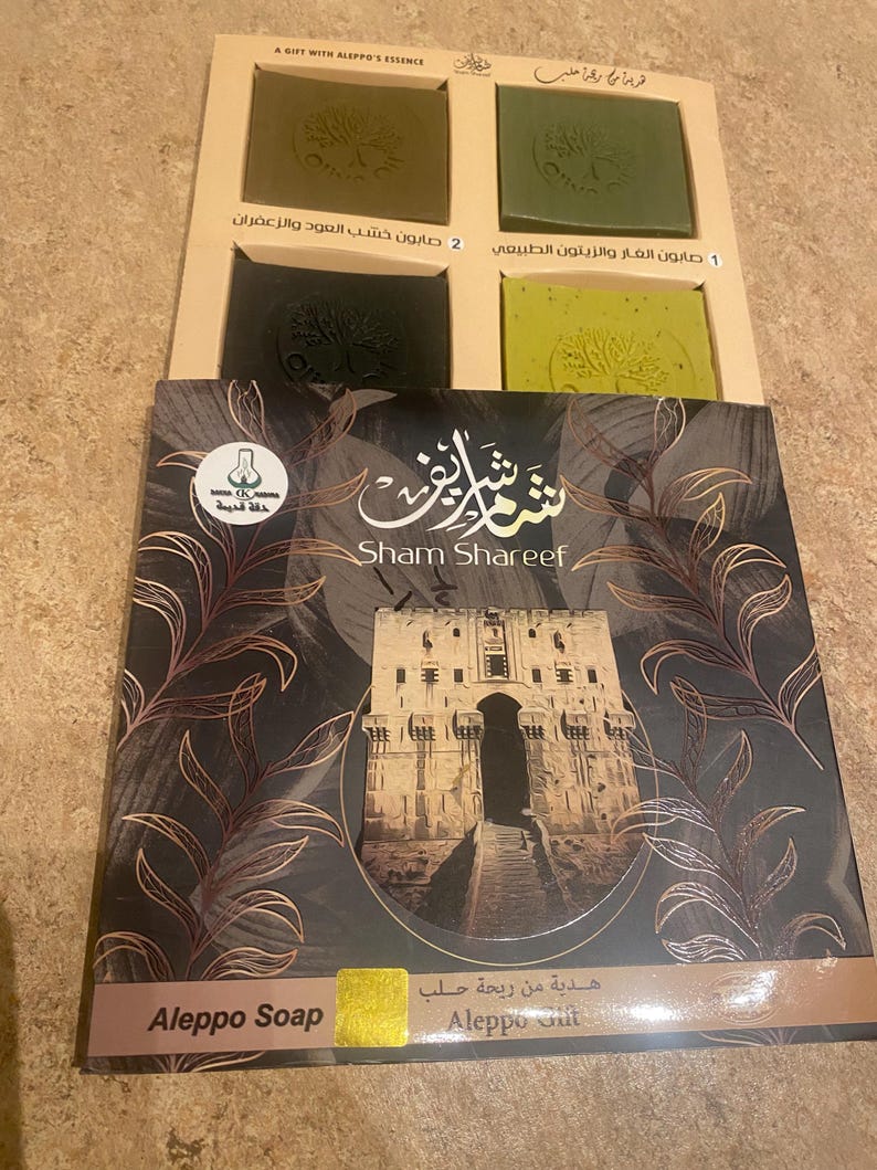 May include: A set of three Aleppo soap bars in a box. The soap bars are green and brown and have a tree design on them. The box is brown and has the words "Sham Shareef" and "Aleppo Soap" on it.
